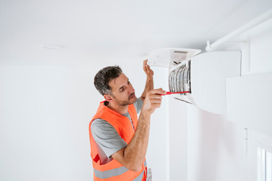 Mature technician repairing air conditioner at home