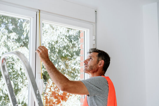 Mature technician measuring window at home