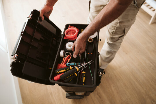 Mature technician picking up tools from box at home