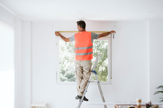 Mature repairman measuring window in house under renovation