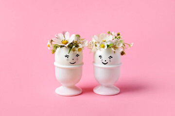 White eggs with funny face in a stand with spring pear and strawberry flowers on a pink background....