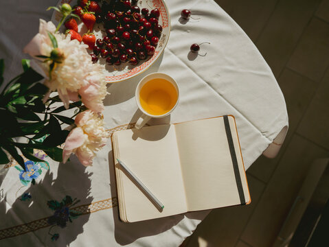 Open diary near teacup and cherries on table at home