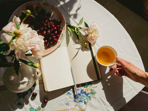 Hand of woman holding teacup near diary on table at home