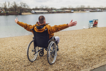 Rear view image of paraplegic handicapped man in wheelchair by the lake. He is enjoying outdoor.