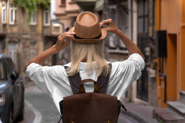 Photo from the back of a young blonde woman with a backpack holding her hat with her hands on a beautiful street in Istanbul,Turkey. Stylish girl walks along an atmospheric city street, travel