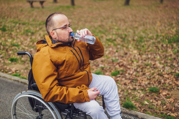 Paraplegic handicapped man in wheelchair is enjoying outdoor and drinking water.