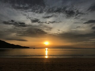 fishing boat is floating right in the middle of the ray of sunset over the sea with twilight moment up in the sky and on the beach