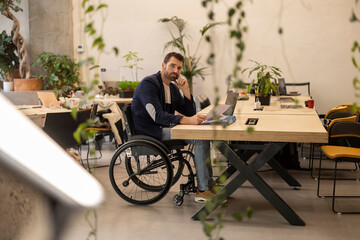 Mature businessman in wheelchair sitting with document at desk