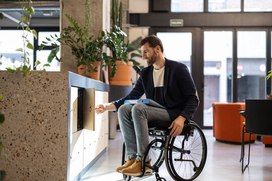 Businessman in wheelchair with disability opening cabinet at workplace