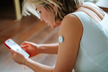 Glucose sensor attached on woman's arm using smart phone at home