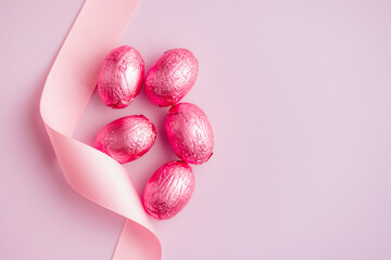 Easter chocolate eggs wrapped in aluminium foil on pink background. Top view.