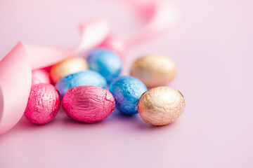 Easter chocolate eggs wrapped in aluminium foil on pink background.