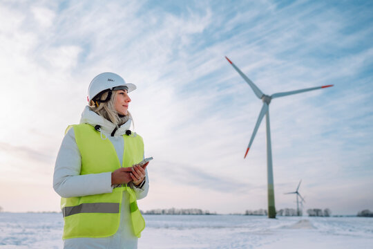 Engineer wearing hardhat holding smart phone standing at wind farm