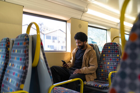 Smiling man using smart phone sitting on subway train seat