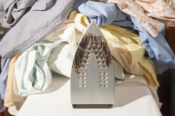 An iron with a burnt sole against the backdrop of a large pile of crumpled laundry. Concept of...