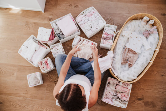 Expecting pregnant woman arranging baby clothes near moses basket at home