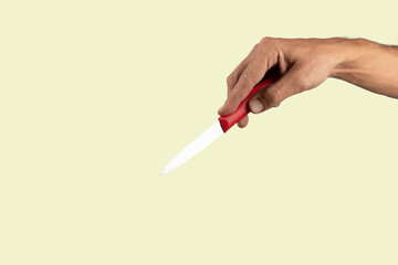 Black male hand holding a red cooking knife isolated on light green background.