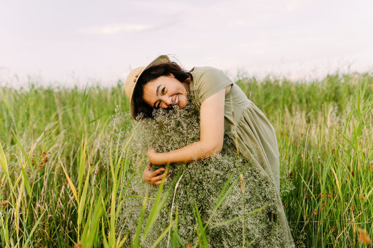 Happy woman embracing gypsophila flowers amidst grass in field
