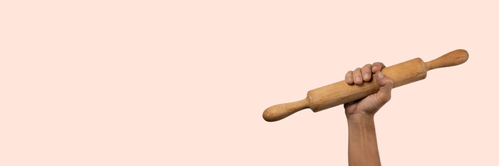 Hand holding a wooden rolling pin isolated on light pink banner background