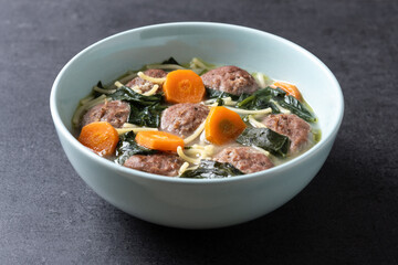 Italian Wedding Soup with meatballs and spinach on black background