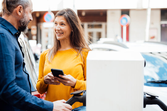 Happy couple talking at electric vehicle charging station