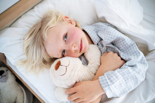 Smiling boy embracing teddy bear on bed at home