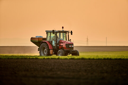 Tractor spreading fertilizer on field at sunset