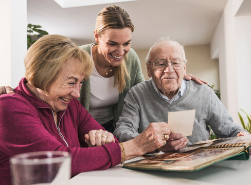 Happy home caregiver with senior couple looking at photographs