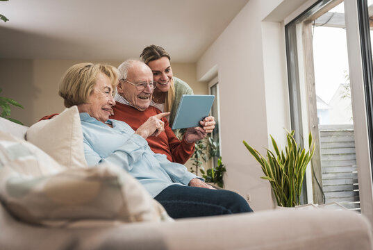 Happy senior couple and home caregiver using tablet PC in living room
