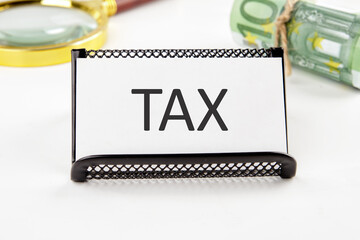 TAX the text on the business card next to the roll of money with a magnifying glass in the background is out of focus on a white background
