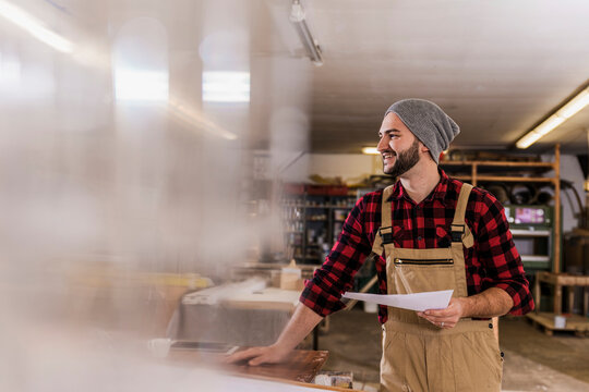 Smiling carpenter holding document at workshop
