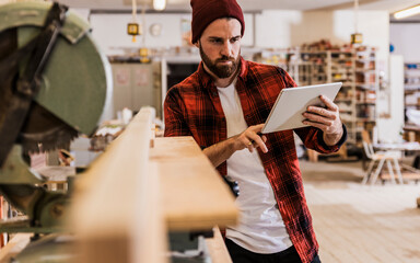 Young carpenter using tablet PC by machinery at workshop