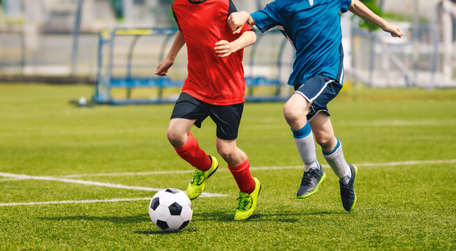Two soccer players chase a soccer ball in a duel. Boys play soccer match on the grass pitch. Football academy players compete in school tournament. Youth footballers running and kicking ball