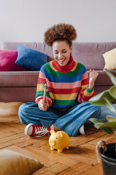 Happy young woman breaking piggy bank with hammer