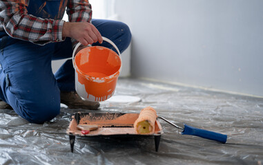 Close-up of male hands pouring paint into the tray. Professional interior painter worker pouring orange color paint to tray.