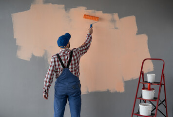 Rear view of painter man painting the wall with paint roller in orange colour, isolated on empty space with red ladder