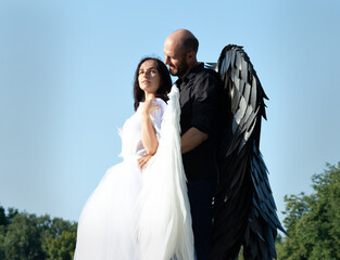 Portrait of a girl in a white dress with white wings and a man with black wings. Couple standing in...