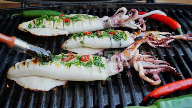 Squids on the cast iron grill barbecue, coat with sauce. Seafood. Squids on grill. Close up