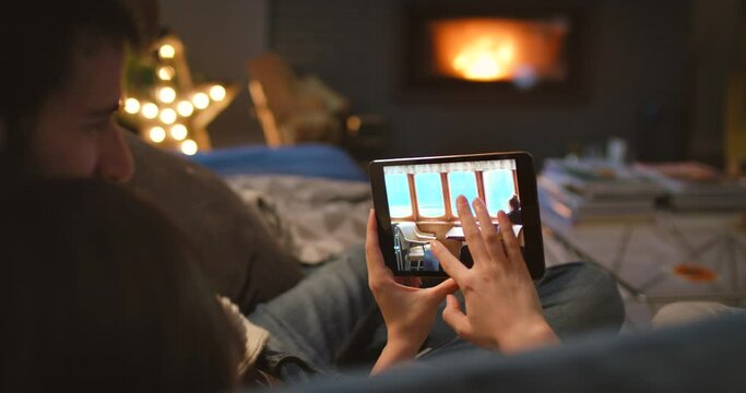 Hands, tablet picture and memory with couple on sofa in living room of home from back at night. Technology, love or travel photographs with man and woman browsing online album of vacation or holiday