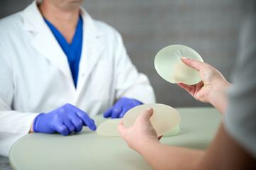 Close-up of female plastic surgeon demonstrates breast implants to a patient for her new breast....