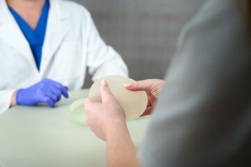 Close-up of female plastic surgeon demonstrates breast implants to a patient for her new breast. The plastic surgeon holds breast silicone implants. Breast augmentation concept. Breast Implant Samples