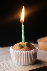 Tasty cupcake kept on a book with a birthday candle on a dark background