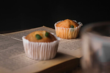 Tasty cupcake kept on a book with a birthday candle on a dark background