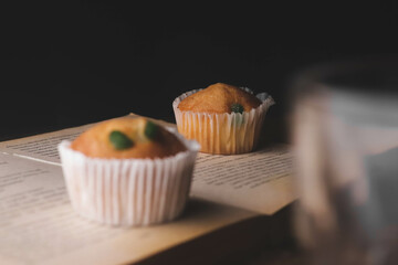 Tasty cupcake kept on a book with a birthday candle on a dark background