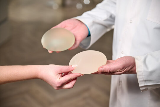 Close-up of female plastic surgeon demonstrates breast implants to a patient for her new breast. The plastic surgeon holds breast silicone implants. Breast augmentation concept. Breast Implant Samples