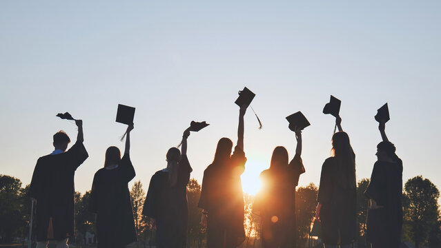 Silhouettes of college graduates waving their caps at sunset.