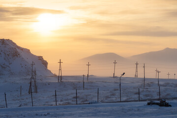 Winter sunset Arctic landscape with electric poles in the snow-covered tundra on the background of mountains. Electric power and ecology in the far North of Russia. Cold weather. Chukotka, Russia.