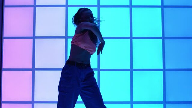 Super slow motion of young in casual colourful wear urban hip-hop female dancer is performing street style choreography on animated luminous neon display radiant neon panels background.