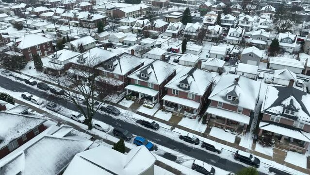 Cinematic drone flight over snow covered american village after snowstorm at night. Snow capped parking cars. Beautiful small town in USA at christmas time. Aerial top down flyover.