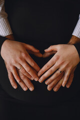 Pregnant woman and her husband which makes heart shape with hands on pregnant belly